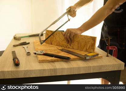 Carpenter cutting a board with a handsaw on the table