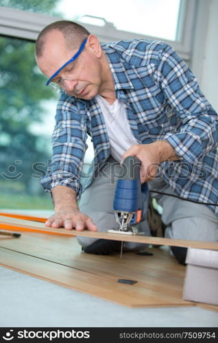 carpenter cutting laminated planks for layered parquet using bandsaw