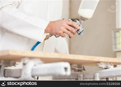 Carpenter in his paint room spraying a piece of wood to be used in his workshop later