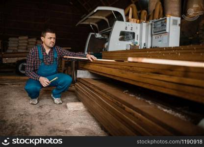 Carpenter in uniform at his workplace on sawmill, woodworking machine on background, lumber industry, carpentry. Wood processing on factory, forest sawing in lumberyard