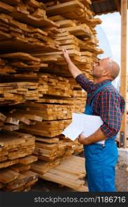 Carpenter in uniform check boards on sawmill, lumber industry, carpentry. Wood processing on factory, forest sawing in lumberyard, warehouse outdoor. Carpenter in uniform check boards on sawmill