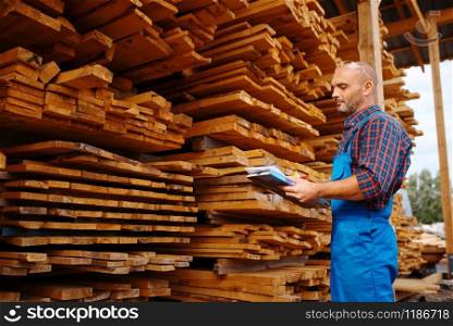 Carpenter in uniform check boards on sawmill, lumber industry, carpentry. Wood processing on factory, forest sawing in lumberyard, warehouse outdoor