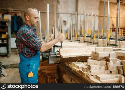 Carpenter in uniform clamps the board in a vise, woodworking, lumber industry, carpentry. Wood processing on furniture factory, production of products of natural materials