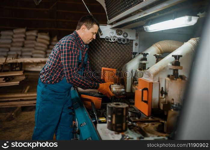 Carpenter in uniform near woodworking machine, lumber industry, carpentry. Wood processing on factory, forest sawing in lumberyard. Carpenter in uniform near woodworking machine
