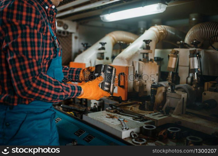 Carpenter in uniform near woodworking machine, lumber industry, carpentry. Wood processing on factory, forest sawing in lumberyard. Carpenter in uniform near woodworking machine