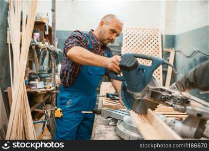 Carpenter in uniform works on circular saw, woodworking, lumber industry, carpentry. Wood processing on furniture factory, production of products of natural materials