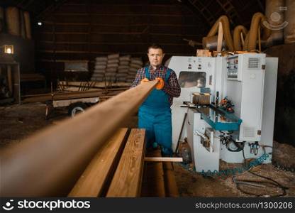 Carpenter in uniform works on woodworking machine, lumber industry, carpentry. Wood factory. Carpenter works on woodworking machine, lumber