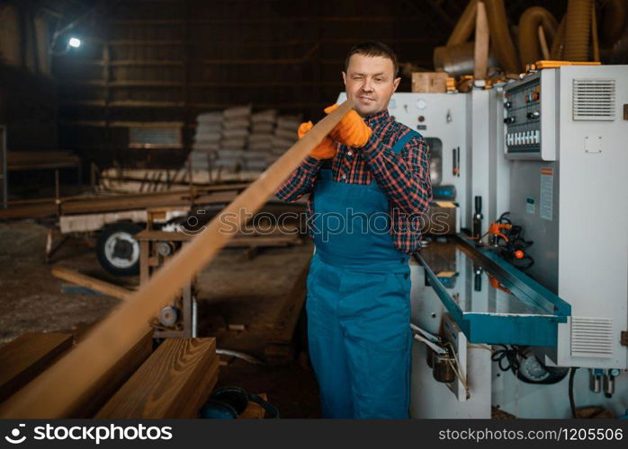 Carpenter in uniform works on woodworking machine, lumber industry, carpentry. Wood processing on factory