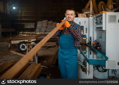 Carpenter in uniform works on woodworking machine, lumber industry, carpentry. Wood processing on factory