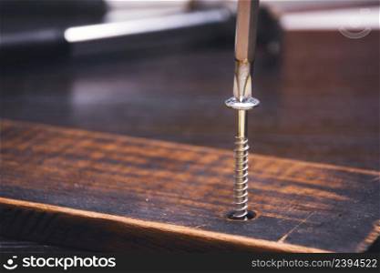 Carpenter is fasten bolt with a cross screwdriver into a hardwood board on the wooden table