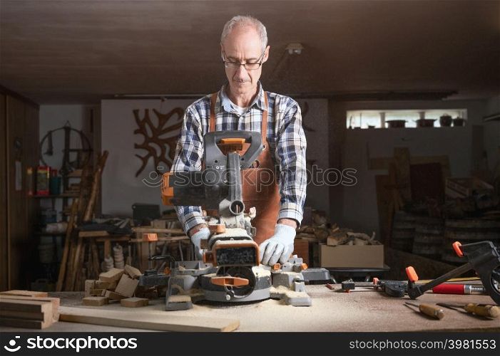 Carpenter is sawing a wood plank with electric circular saw machine in carpentry workshop. Workwood DIY concept. High quality photography.. Carpenter is sawing a wood plank with electric circular saw machine in carpentry workshop. Workwood DIY concept