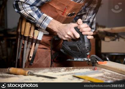 Carpenter is sawing a wood plank with electric jig saw machine in carpentry workshop. Workwood DIY concept. High quality photography.. Carpenter is sawing a wood plank with electric jig saw machine in carpentry workshop. Workwood DIY concept