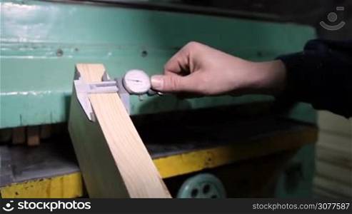 Carpenter measures thickness of wooden board with calipers at carpentry shop closeup. Process of measuring wooden slot with calipers before starting to work in workshop.