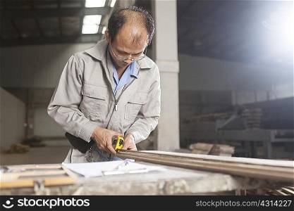 Carpenter measuring wood plank with tape measure in factory, Jiangsu, China