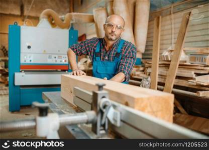 Carpenter processes wooden beam on plane machine, woodworking, lumber industry, carpentry. Wood processing on furniture factory. Carpenter processes wooden beam on plane machine