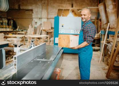 Carpenter processes wooden beam on plane machine, woodworking, lumber industry, carpentry. Wood processing on furniture factory, production of products of natural materials. Carpenter processes wooden beam on plane machine