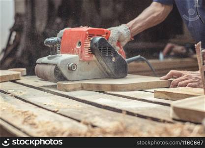 Carpenter sanding wood with belt sander at workshop in wooden cutting board project or woodworking carpentry
