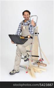 Carpenter sitting on a stepladder with a laptop computer