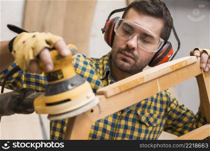 carpenter softening edges wooden furniture with electric sander