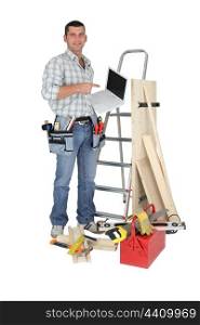 Carpenter stood by ladder with laptop