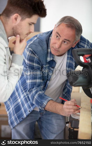 carpenter teaching apprentice standing in joinery workshop