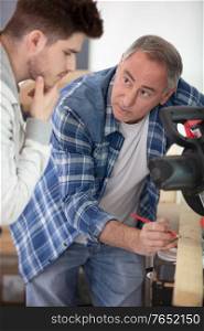 carpenter teaching apprentice standing in joinery workshop
