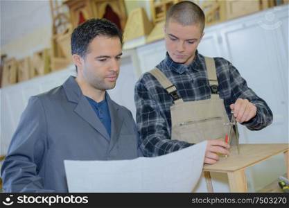 carpenter with apprentice looking at plans in workshop