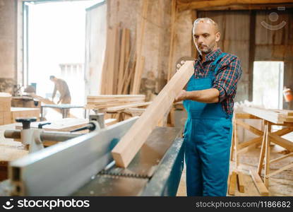 Carpenter with board near plane machine, woodworking, lumber industry, carpentry. Wood processing on furniture factory, production of products of natural materials