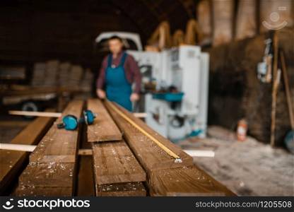 Carpenter with measuring tape measures boards, woodworking machine on background, lumber industry, carpentry. Wood processing on factory, forest sawing in lumberyard