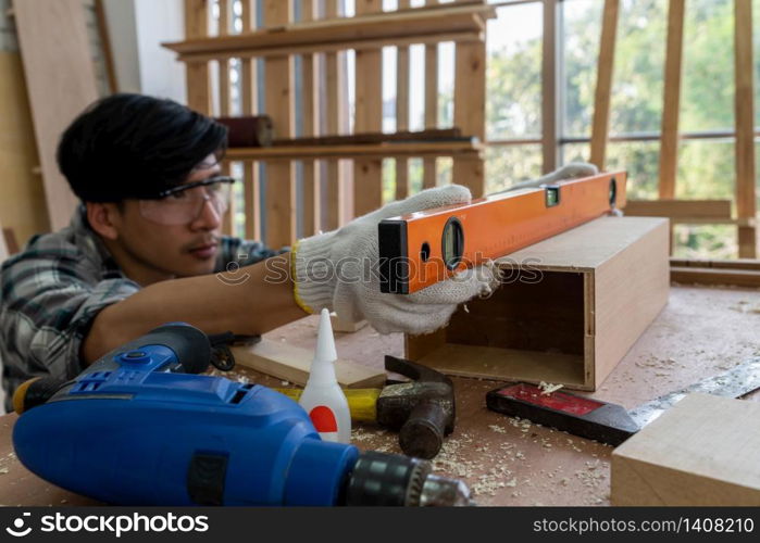 Carpenter working on wood craft at workshop to produce construction material or wooden furniture. The young Asian carpenter use professional tools for crafting. DIY maker and carpentry work concept.