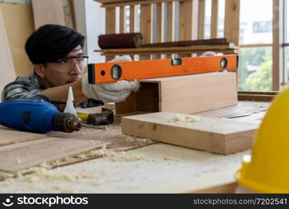 Carpenter working on wood craft at workshop to produce construction material or wooden furniture. The young Asian carpenter use professional tools for crafting. DIY maker and carpentry work concept.