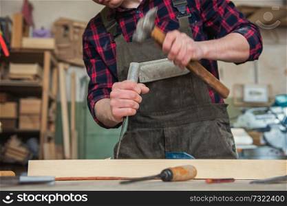 Carpenter working with a chisel and hammer in a wooden workshop. Profession, carpentry and manual woodwork concept.. Carpenter working with a chisel