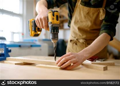 Carpenter working with drill leaning over table at carpentry workshop. Repairman assembling wooden parts using professional instrument. Carpenter working with drill leaning over table at carpentry workshop