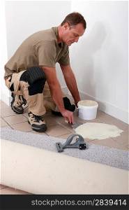 Carpet fitter spreading adhesive on a tiled floor