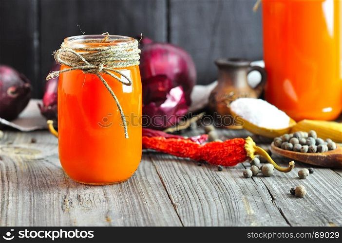 Carrot juice in a glass jar, behind fresh carrots and red onions