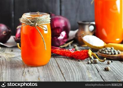 Carrot juice in a glass jar, behind fresh carrots and red onions