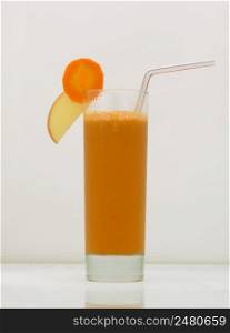 carrot juice in a glass with a straw and a slice of carrot and apple. drink isolated on white background. fruit drinks in a glass