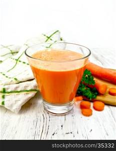Carrot juice in a tall glass, vegetables with parsley, napkin against the background of wooden boards