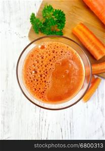 Carrot juice in a tall glass, vegetables with parsley on a background of wooden boards on top