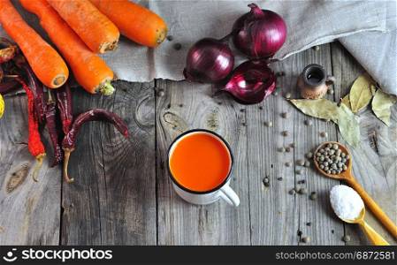 Carrot juice in an iron mug on a gray wooden table, next to a fresh whole carrot