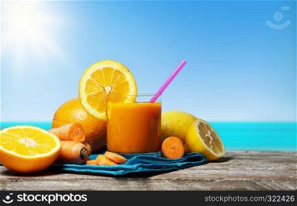 Carrot, orange and lemon juice. Healthy and refreshing fruity summer drink front view on a wooden table with blue sea and sky on background in a beautiful hot summer day.