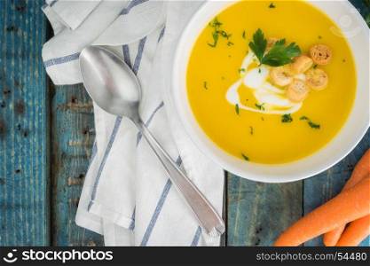 Carrot soup with cream and parsley on wooden background. Copy space