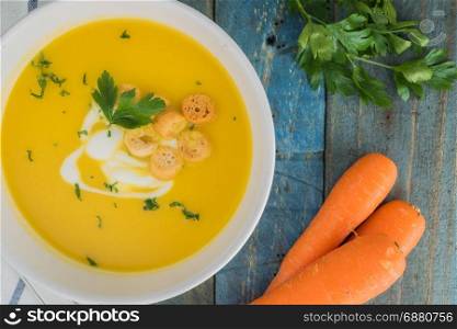 Carrot soup with cream and parsley on wooden background. Copy space