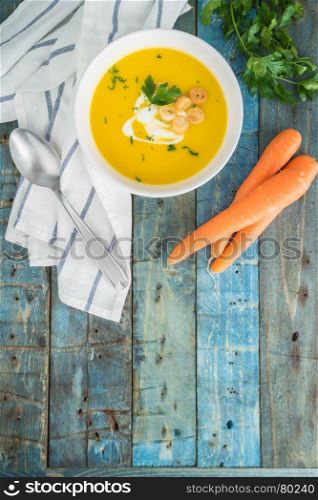 Carrot soup with cream and parsley on wooden background. Top view. Copy space