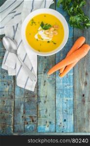 Carrot soup with cream and parsley on wooden background. Top view. Copy space