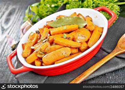 Carrots fried with garlic, bay leaf, spices and green onions in a pan on a napkin, basil and parsley on black wooden board background