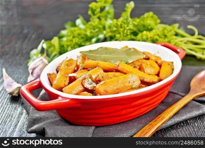 Carrots fried with garlic, bay leaf, spices and green onions in a pan on a napkin, basil and parsley on dark wooden board background
