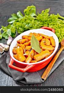 Carrots fried with garlic, bay leaf, spices and green onions in a pan on a towel, basil and parsley on dark wooden board background