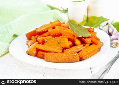 Carrots fried with garlic, bay leaf, spices and green onions in a plate, basil and a napkin on light wooden board background