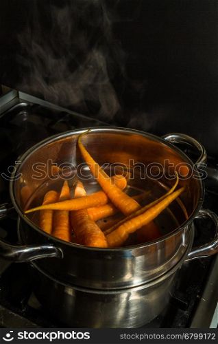 Carrots or Daucus carota in a stainless steel steamer being steamed on a hob.